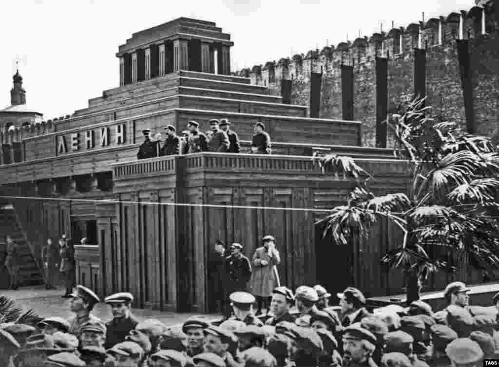 Лидеры большевиков, в том числе Иосиф Сталин (третий справа), на площадке нового мавзолея в 1926 году. В марте 1924 года Щусев построил новый деревянный мавзолей, попросторнее. При эксплуатации первого, площадью поменьше, возникли проблемы: из-за потока посетителей в здании быстро становилось тепло, это, в свою очередь, плохо сказывалось на сохранности останков