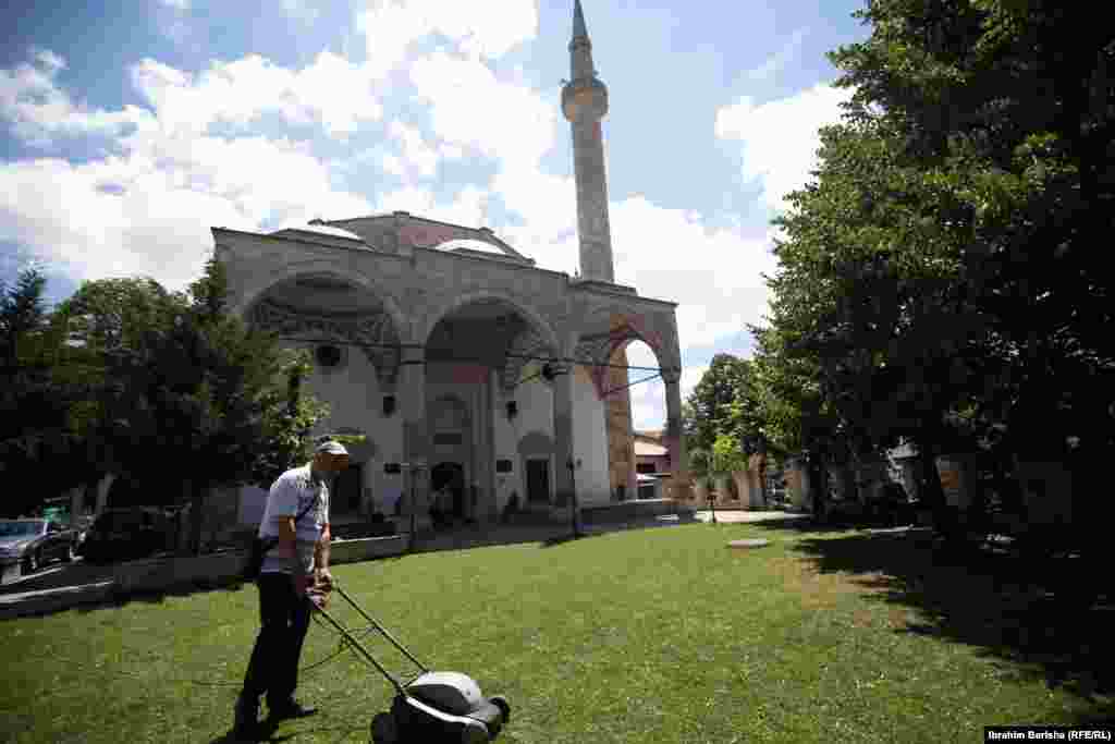 Një burrë kosit barin në kopshtin e Xhamisë së Madhe në Prishtinë.