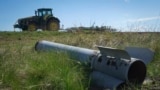 Un fragment dintr-o rachetă rusească zace pe un câmp în timp ce un fermier își lucrează pământul în regiunea Harkov din Ucraina, devastată de război.
