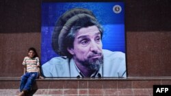 Afghanistan -- An Afghan boy sits next to poster bearing the image of the late resistance leader Ahmad Shah Masud as his fourteenth death anniversary is marked in Kabul, September 9, 2015