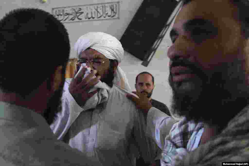 People comfort a cleric who is mourning the loss of students at the madrasah.