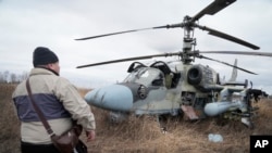 Мужчина стоит перед российским боевым вертолетом Ка-52 в поле после вынужденной посадки под Киевом, Украина, 24 февраля 2022 г. 