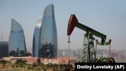 AZERBAIJAN -- Skyscrapers stand in the background as an oil pump works a nearby hill in Baku