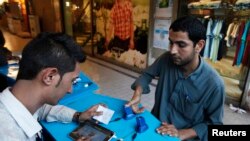 A customer (R) gets his thumb scanned for bio-metric verification on his subscriber identity module (SIM) card.